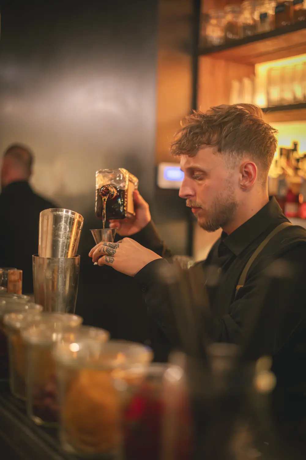Bartender van WonderBar Genk schenkt een huisinfusie in een koperen jigger boven de shaker