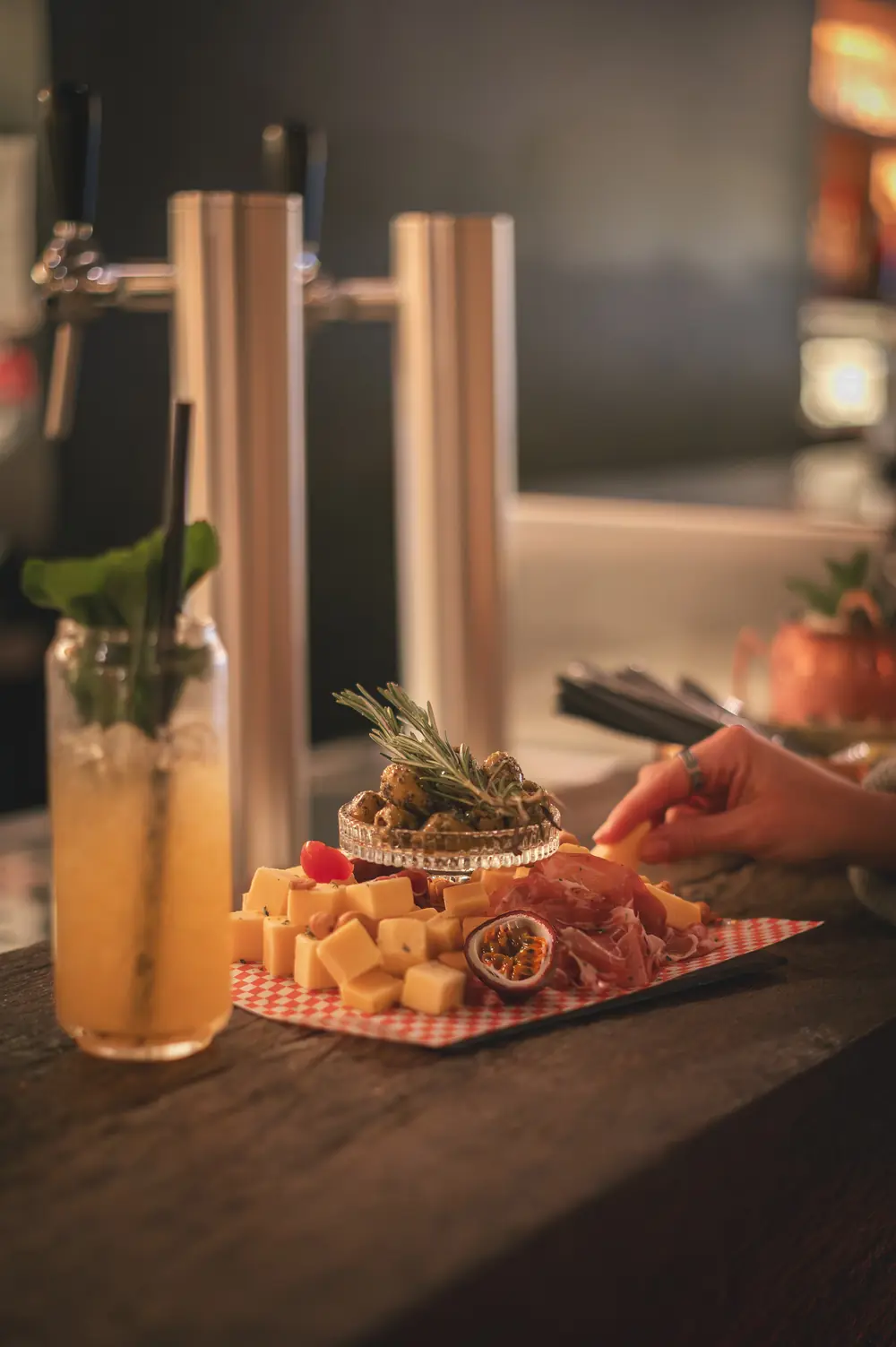 Sharing platter met kaas, vleeswaren, olijven en passievrucht naast een hoge cocktail aan de bar van WonderBar Genk
