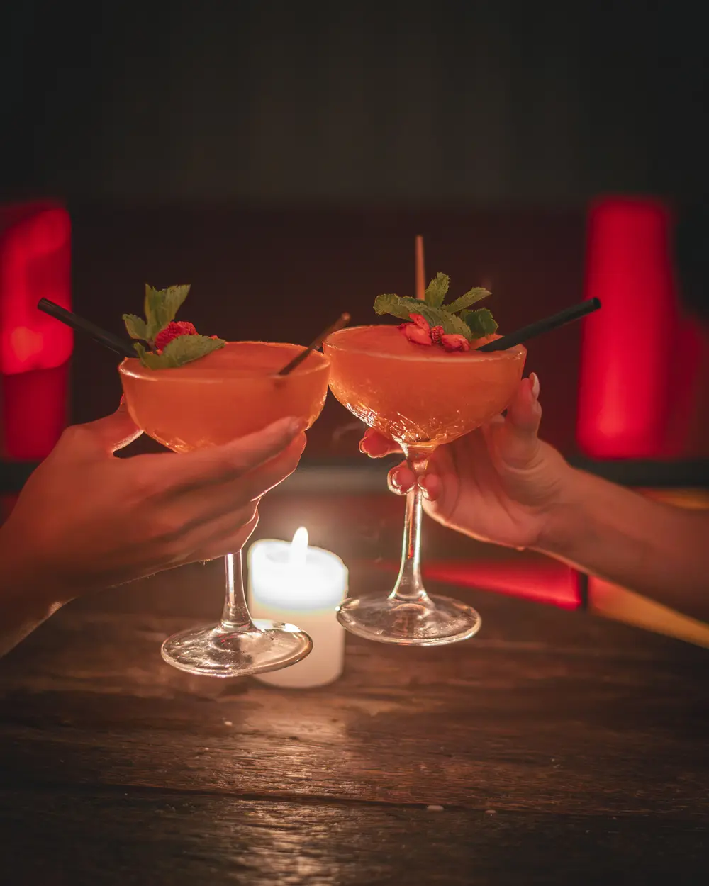Twee gasten klinken met frozen daiquiri-coupes boven een kaars aan een houten tafel in WonderBar Genk