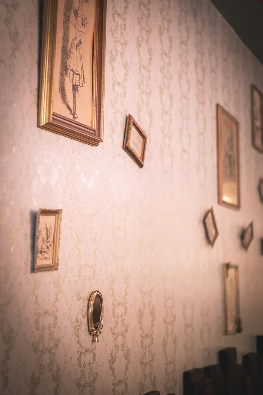 Galerijmuur met gouden lijsten en Tenniel-engravings van Alice in Wonderland tegen damast-behang in WonderBar Genk