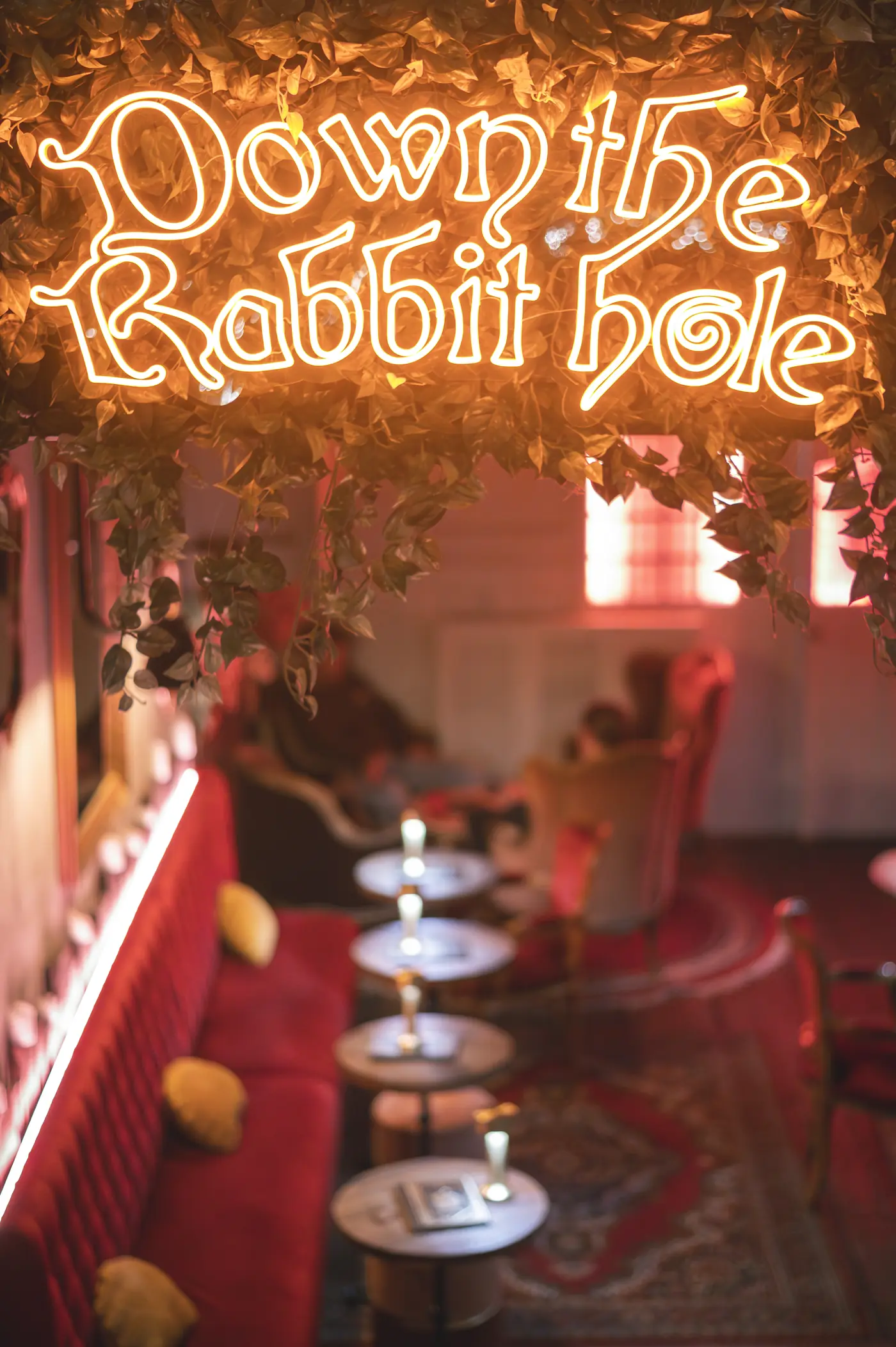 Oranje neon &lsquo;Down the Rabbit hole&rsquo;-bord met klimop boven de rode loungebanken van WonderBar Genk