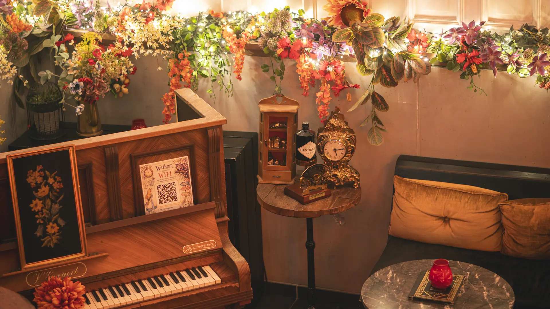 Iconische vintage piano in WonderBar Genk met witte &lsquo;WONDERᙠAR&rsquo;-belettering en gespiegelde B als merksignatuur, omringd door bloemenslinger en marmertafel met rode roos