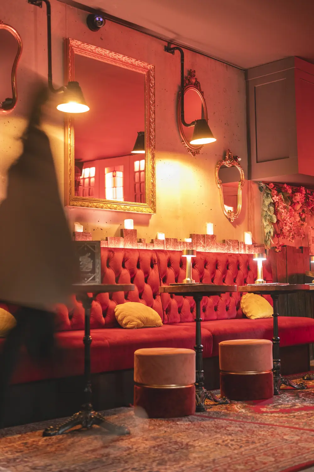 Rode chesterfield-lounge in WonderBar Genk met goud-gerande spiegels, kaarsen op de tafels en fluwelen krukken op het oosterse tapijt