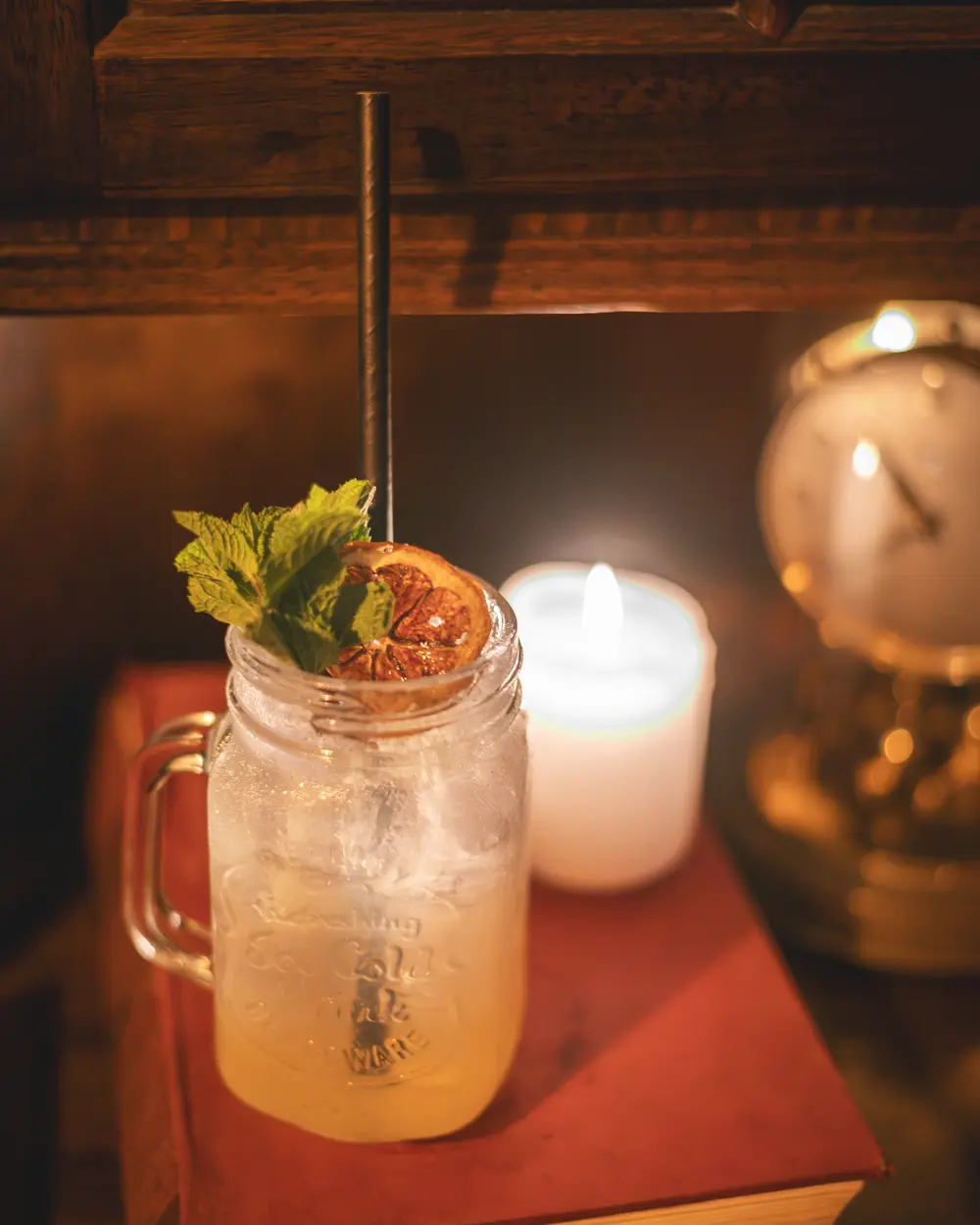 Lynchburg Lemonade in mason jar met munt en gedroogde sinaasappel op een antiek boek naast een koperen klok in WonderBar Genk